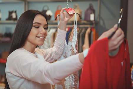 在服装店买衣服的迷人年轻女子折扣设计师市场织物产品镜子零售闲暇消费者销售